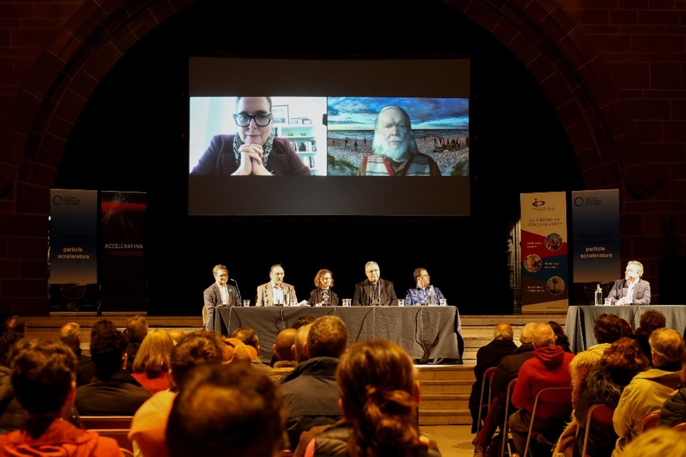 A group of people sitting at a table during a panel discussion in front of a crowd of people.
