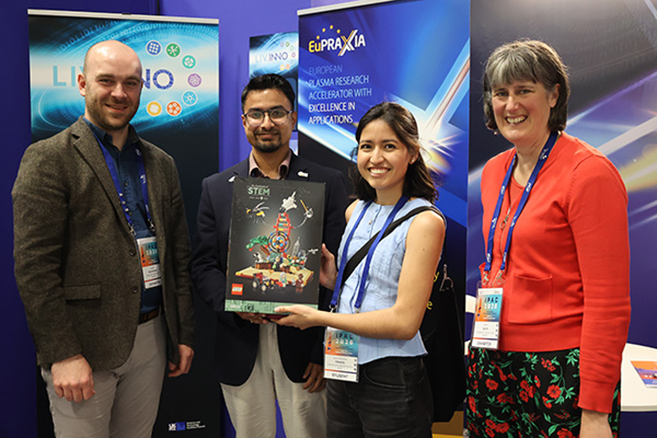 Four people posing for a picture. One is holding a lego set on their hands.