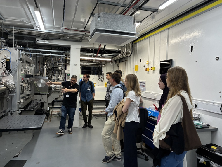 A person in the lab next to a big set up, explaining something to a group of students.