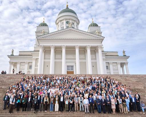A large group of people posing for a picture. They are standing on steps in front of a large white building.